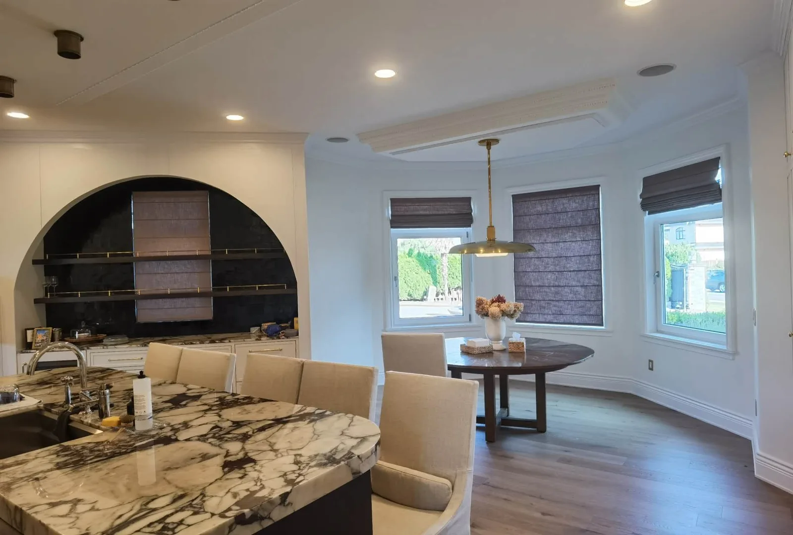 Roman shades partly raised around a dining bay and kitchen window
