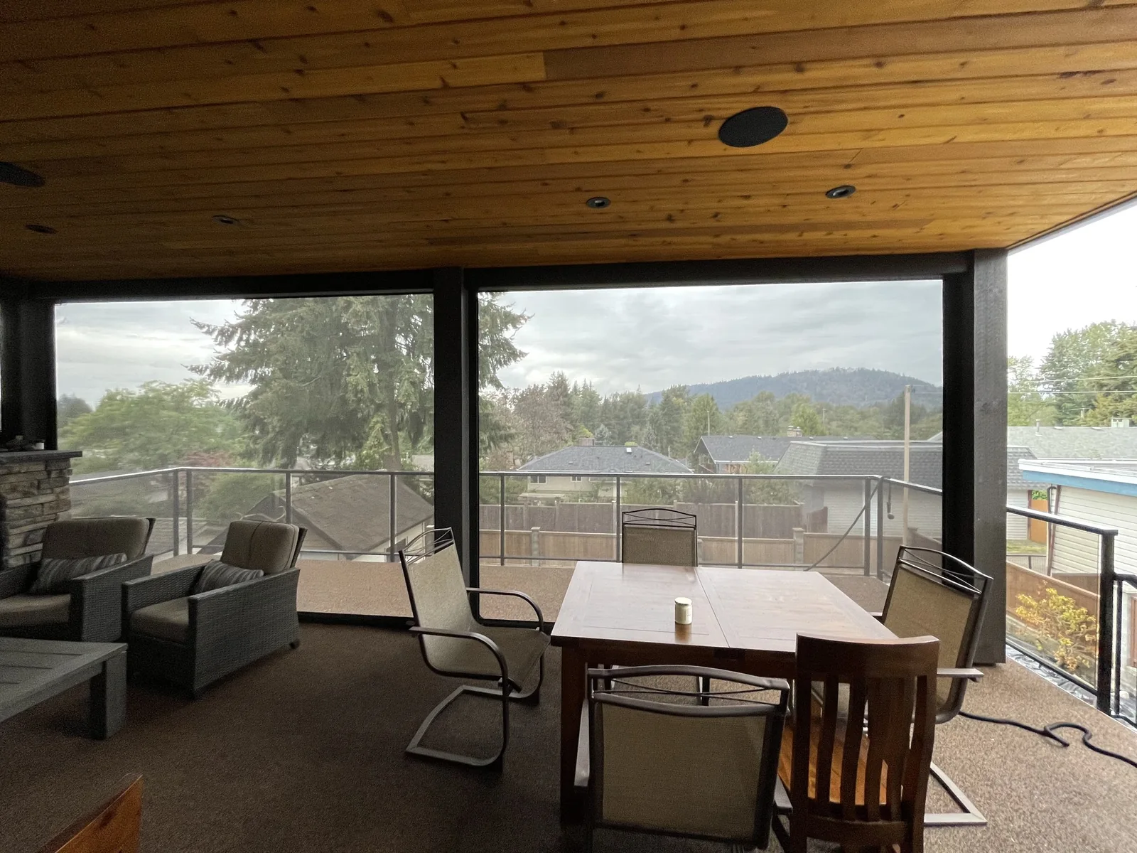AAA Blinds motorized outdoor roller shades around a covered patio, with trees and hills visible through the mesh